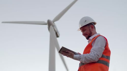 An Electrical Engineer Looks at a Modern Digital Tablet and Raises His Hand with an Orange Battery