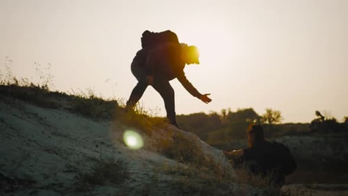 Man Helping Woman Hike in Rural Sunset