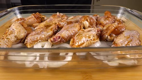 Die marinierten Hähnchenflügel werden auf den Zwiebelringen in einer Glasauflaufform ausgelegt.