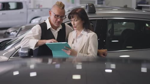 Un couple marié caucasien réussi examine les nouvelles caractéristiques du véhicule sur une tablette debout dans une voiture