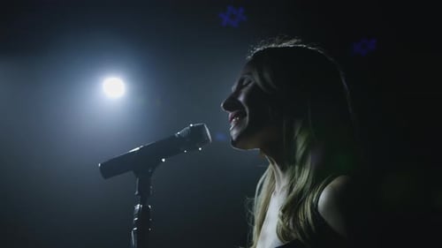 Close-up of the Face of the Singer with Microphone on a Black Smoky Background. The Singer Sings a