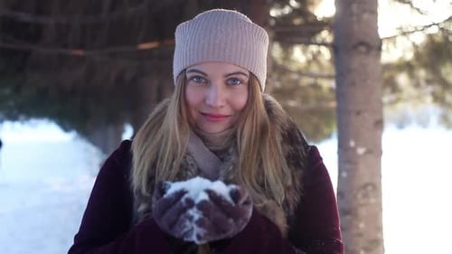 Young Woman Blowing Snow In Winter Forest