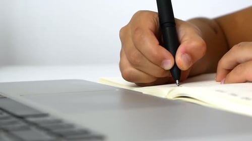 Close Up of Person Writing in Notebook at Desk