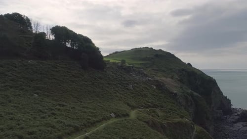 Low aerial tracking forward above the green grass above Wringcliff bay next to the valley of rocks,
