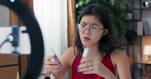 Bloguera de belleza femenina filmando tutorial de rutina diaria de maquillaje usando luz anular con teléfono en trípode