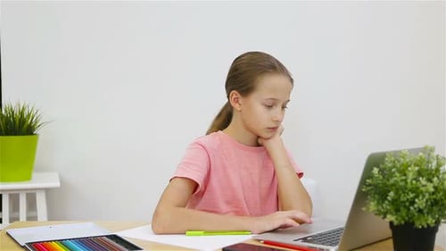Ernsthaftes Schulmädchen sitzt mit Laptop und Lehrbuch am Tisch und macht Hausaufgaben. Von zu Hause aus lernen