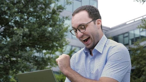 Man Cheers Success on Laptop in Urban Setting