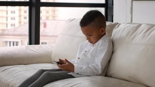 Child Using Smartphone While Sitting on a Couch