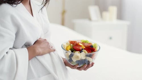 Pregnant Woman with Fruit Bowl in Bedroom