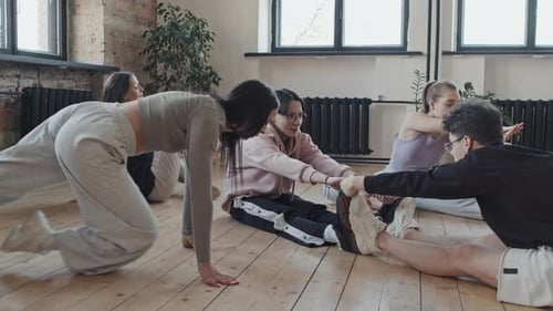 Young Adults Stretching Together on Wooden Floor