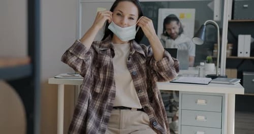 Slow Motion Portrait of Attractive Brunette Putting on Face Mask and Looking at Camera in Office
