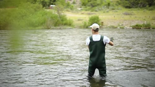 Slow Motion Shot of a Caucasian male fisherman casting his hook while Fly Fishing. He is standing in