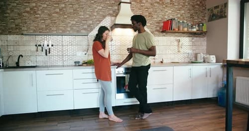 Young Couple Talk and Drink Stand Barefoot at Kitchen