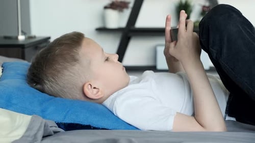 Child Lies on Bed Playing Mobile Phone