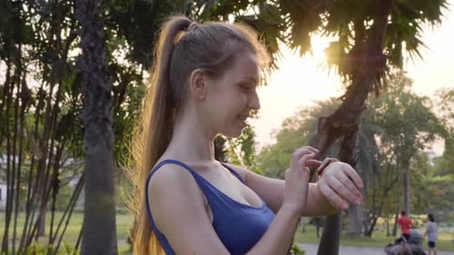 Athletic Woman Checks Smartwatch in Golden Hour Park