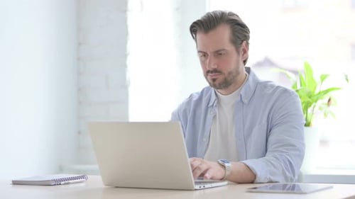 Man Coughing While Using Laptop at Desk