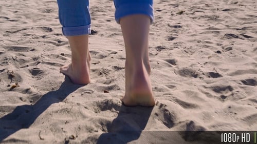 Following Behind a Woman Stepping in Sandy Seacoast Beach on a Sunny Day Close-Up on the Feet