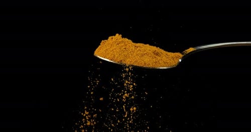 Spoon and Curry Powder falling against Black Background, Slow motion 4K