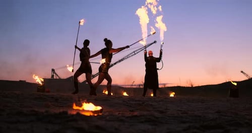 Eine Gruppe von Männern und Frauen Feuershow bei Nacht im Sand vor dem Hintergrund von Feuer und Turm