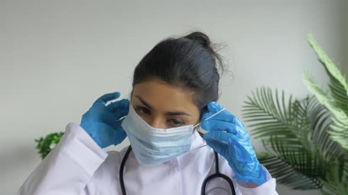 Portrait of A Young Woman Doctor Wearing A Mask Rubber Gloves Against The Virus in A Bright Office