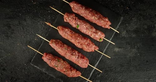 Raw Kebab Sausages on a Stick on a Stone Board Rotate.
