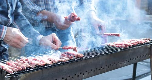 Adults Grilling Meat Skewers Over Barbecue