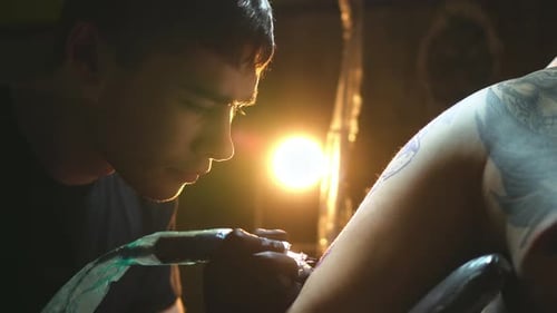 Young Man Tattooing Arm in Dark Studio