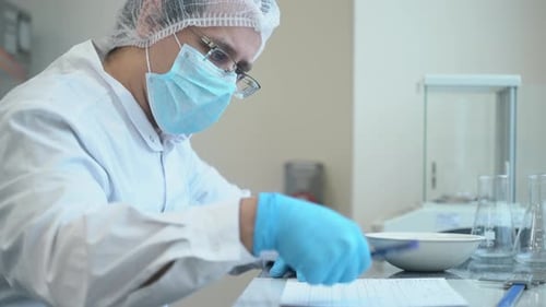 Travailleur pharmaceutique pesant un comprimé sur une balance de contrôle. Il note les chiffres
