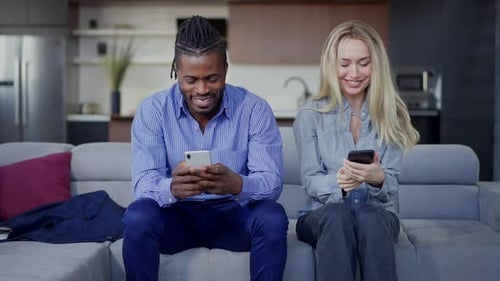 Smiling Man and Woman Sit on Sofa with Phones