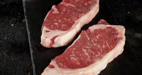 Two Raw Steaks Displayed on Black Surface