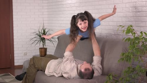 Girl Pretends Flying with Father on Couch