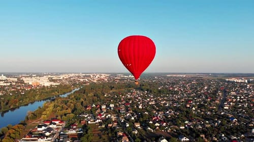 A beautiful red balloon flies in the evening over the river and the city.