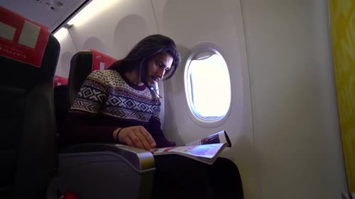 Man Reading on Airplane Seated by Window