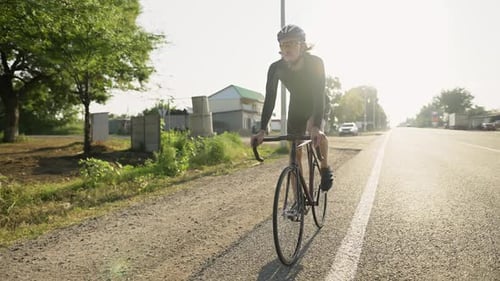 A Male Professional Cyclist Rides Bicycle Along the Country Side Road