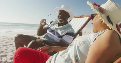 Smiling senior african american couple lying on sunbeds on sunny beach