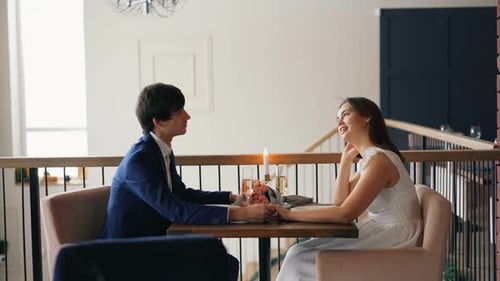 Happy Couple Young Man and Woman Are Talking Holding Hands Sitting in Restaurant on Date Together