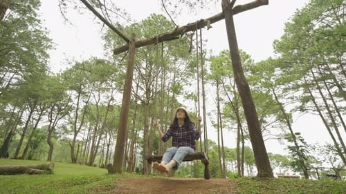 Happy Asian woman swinging on a swing in forest trees