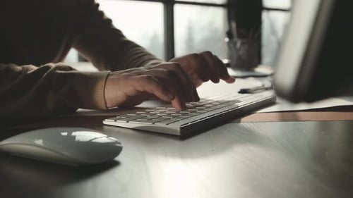 Men's Hands in a Beige Sweater Print on the Keyboard in Light Office