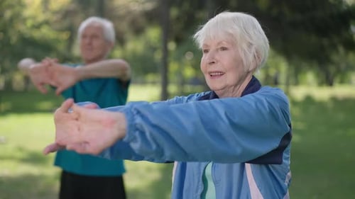 Smiling Senior Sportswoman Stretching Hands Forward with Blurred Sportsman Exercising at Background