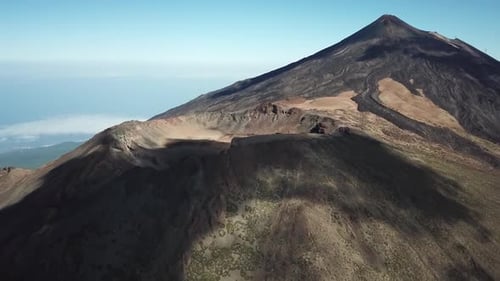 Drohnenclip über die Spitze eines Vulkans mit Wolken, die Schatten hinterlassen