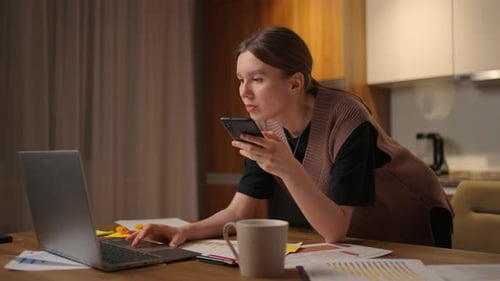 Woman Working at Laptop While Holding Smartphone