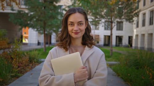 Woman Smiling Holding Laptop in Urban Setting