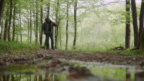 Casual Strong Man Walking with Ax in Wild Deciduous Forest.