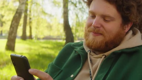 Cheerful Man Using Phone in Park