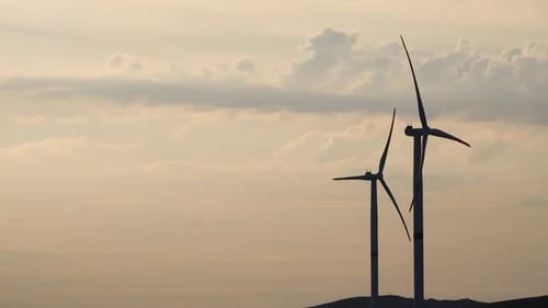 Motion the Blades of a Large Wind Turbine in a Field Against a Background of Orange Sunset on the