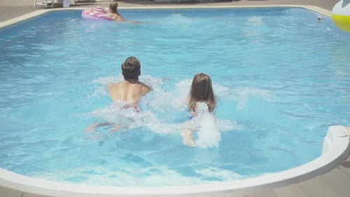 Back View of Young Caucasian Man and Woman Swimming in Outdoor Water Pool at Luxurious Resort