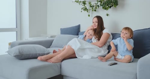Children Hug Mom Sitting on the Couch and Watching TV
