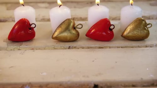 Burning candles with heart shape pendant on wooden plank