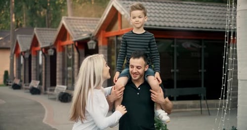 Parents Are Carrying the Son on Shoulders As They Walk in a Park