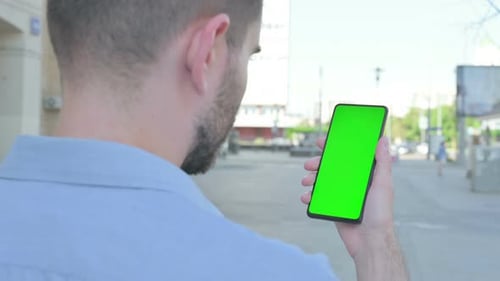 Young Man Using Smartphone with Green Screen Outdoor